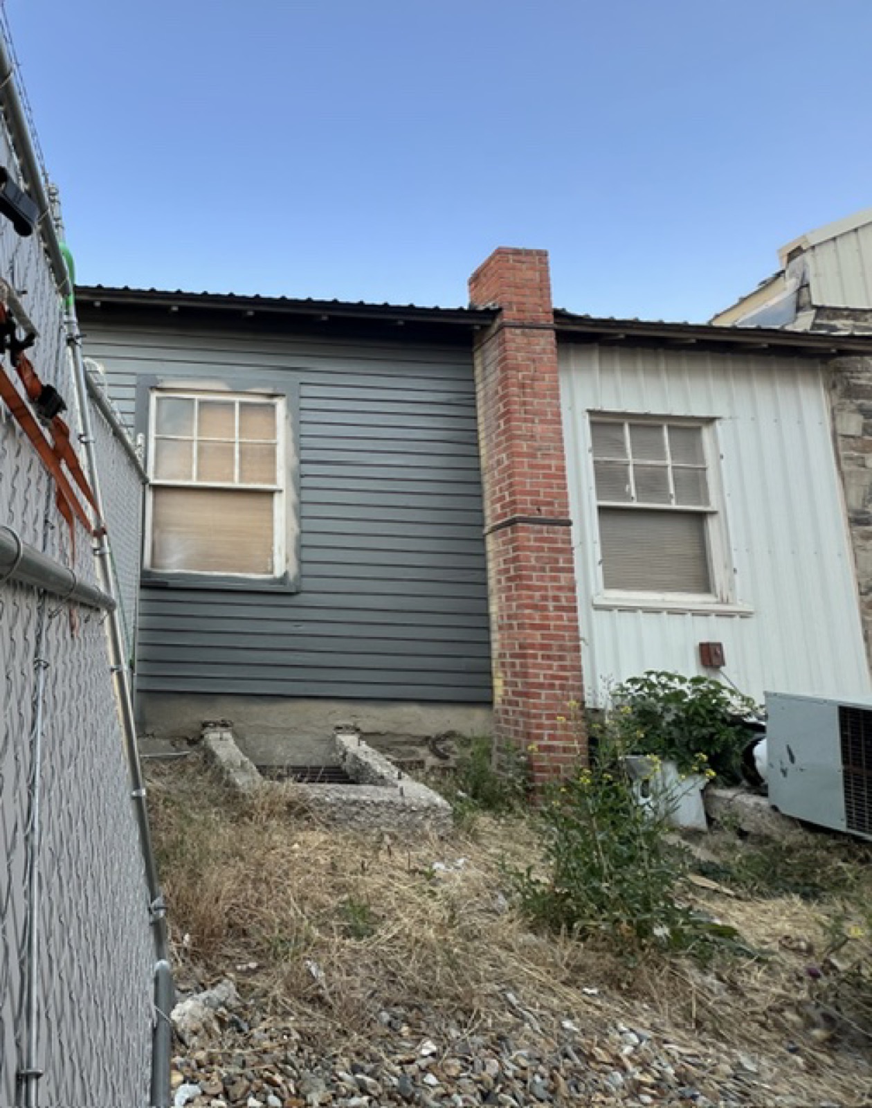 Clapboard office wall and corrugated metal, six-pane windows, a concrete well in the foreground