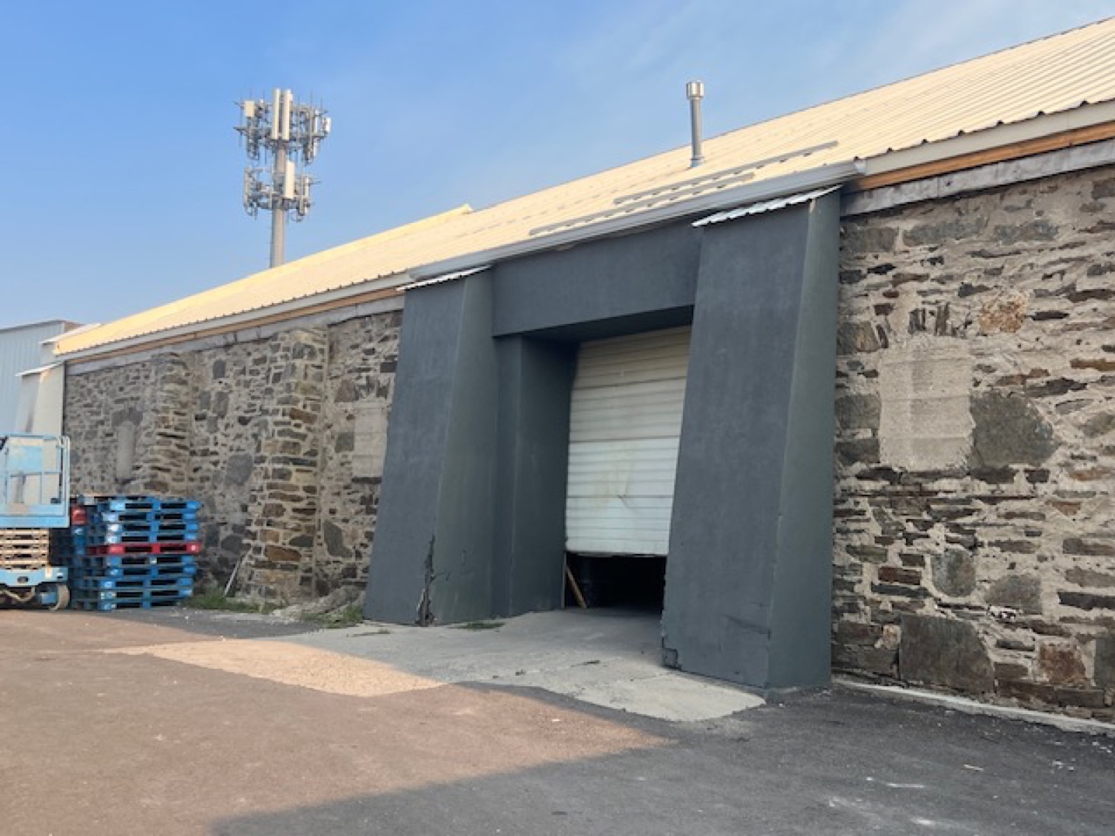 Stone wall with a modern loading portal, a white roll-up door partly open, pallets and a lift
