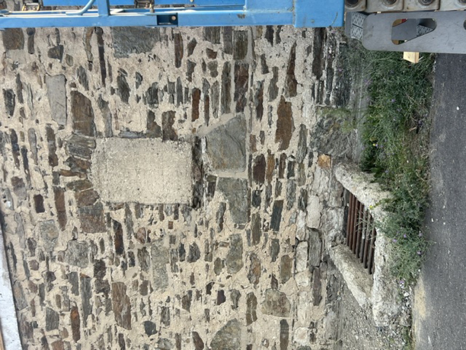 Stone wall with a rectangular repair patch and a barred low opening
